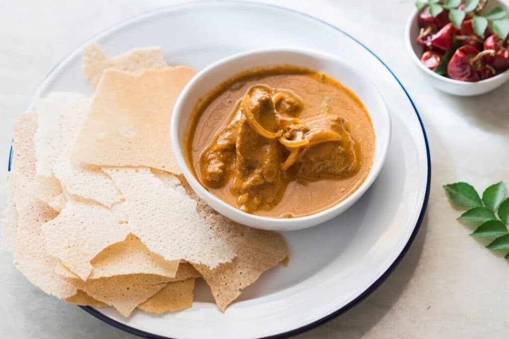 Mangalorean kori rotti: chicken curry in a bowl with crisp rice wafers on the side
