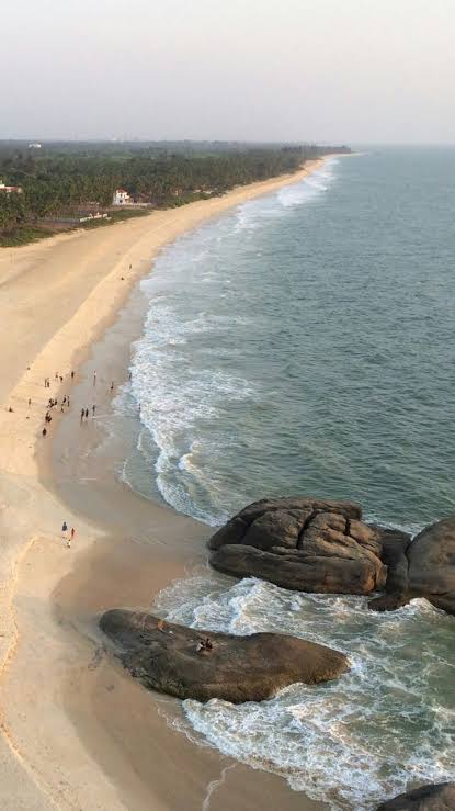 Aerial view of a long sandy beach near Mangaluru with waves breaking on large rocks